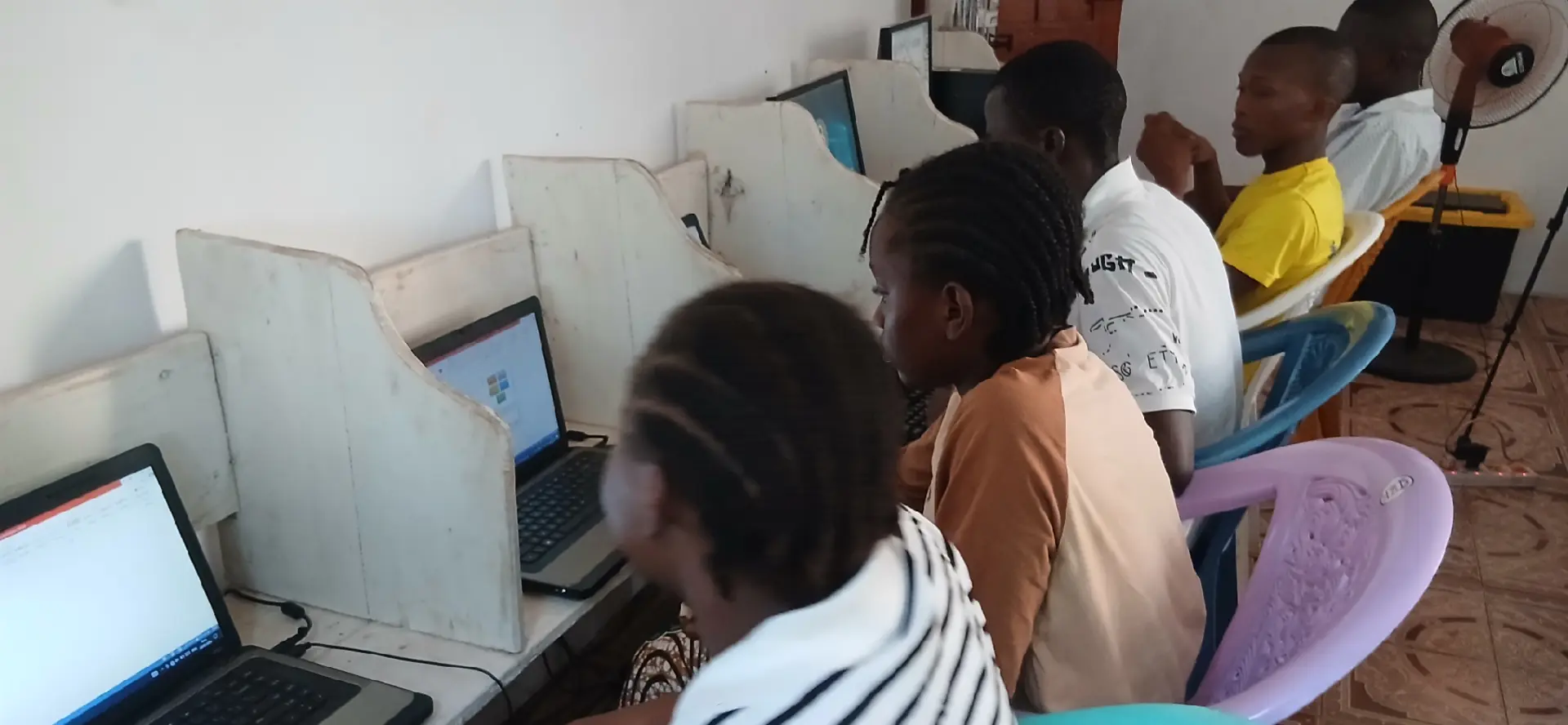 Young women and men working at laptops in individual study booths at a community learning centre