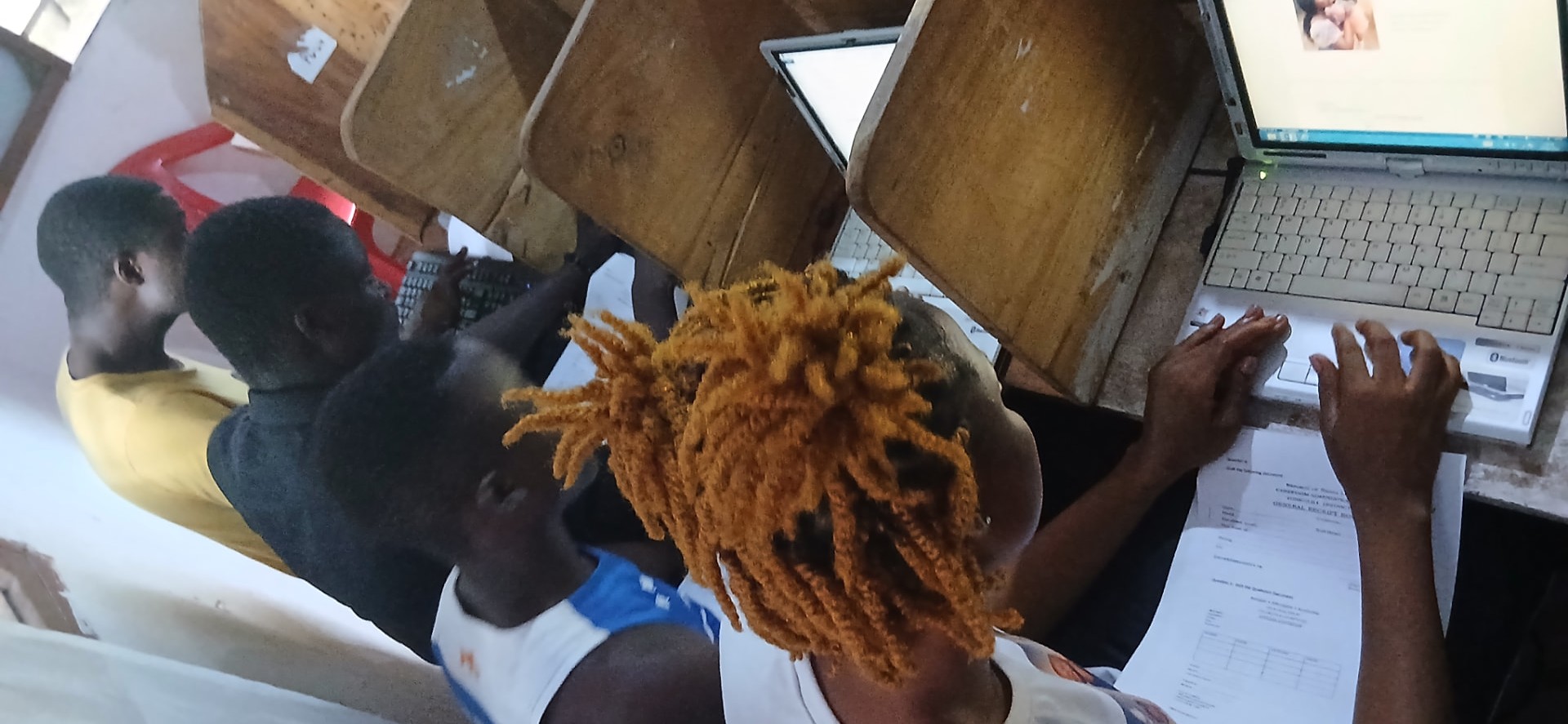 Overhead view of learners typing at laptops with printed assessment papers beside them