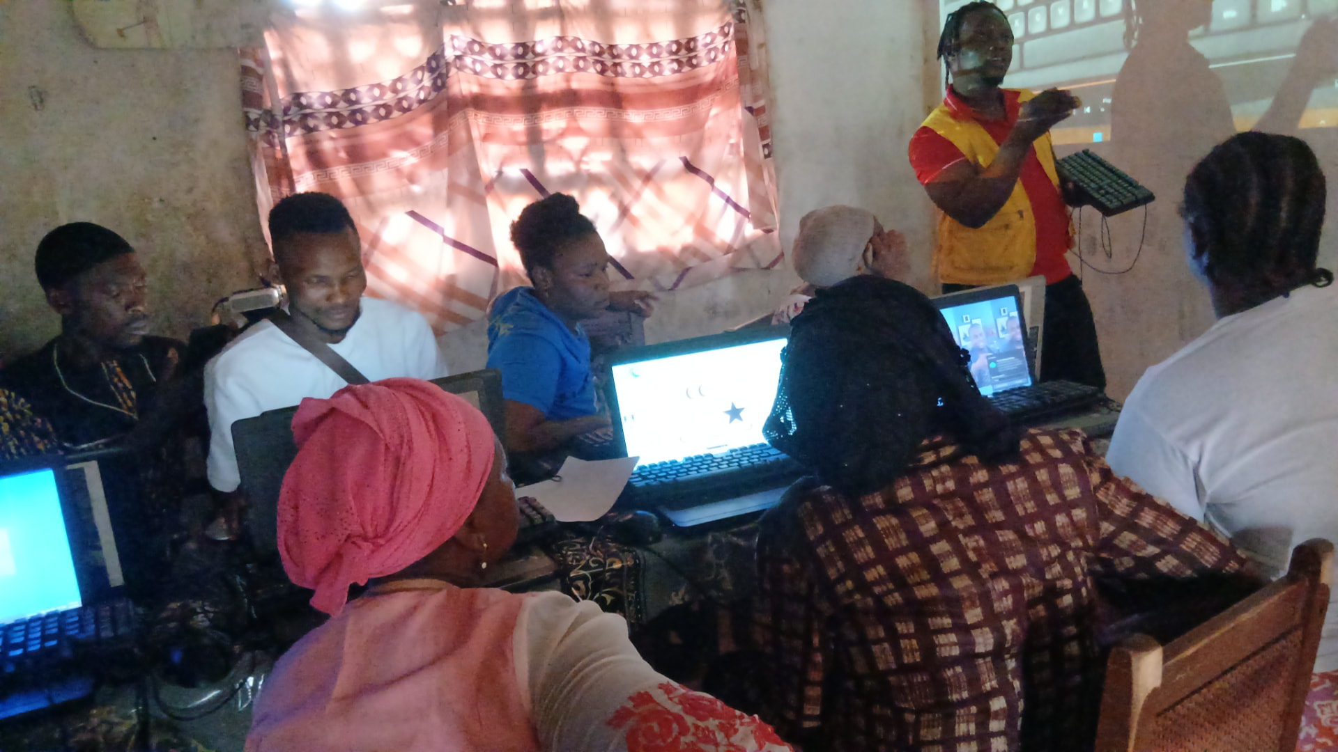 A facilitator explaining a keyboard on a projector screen to a group of adult learners at laptops