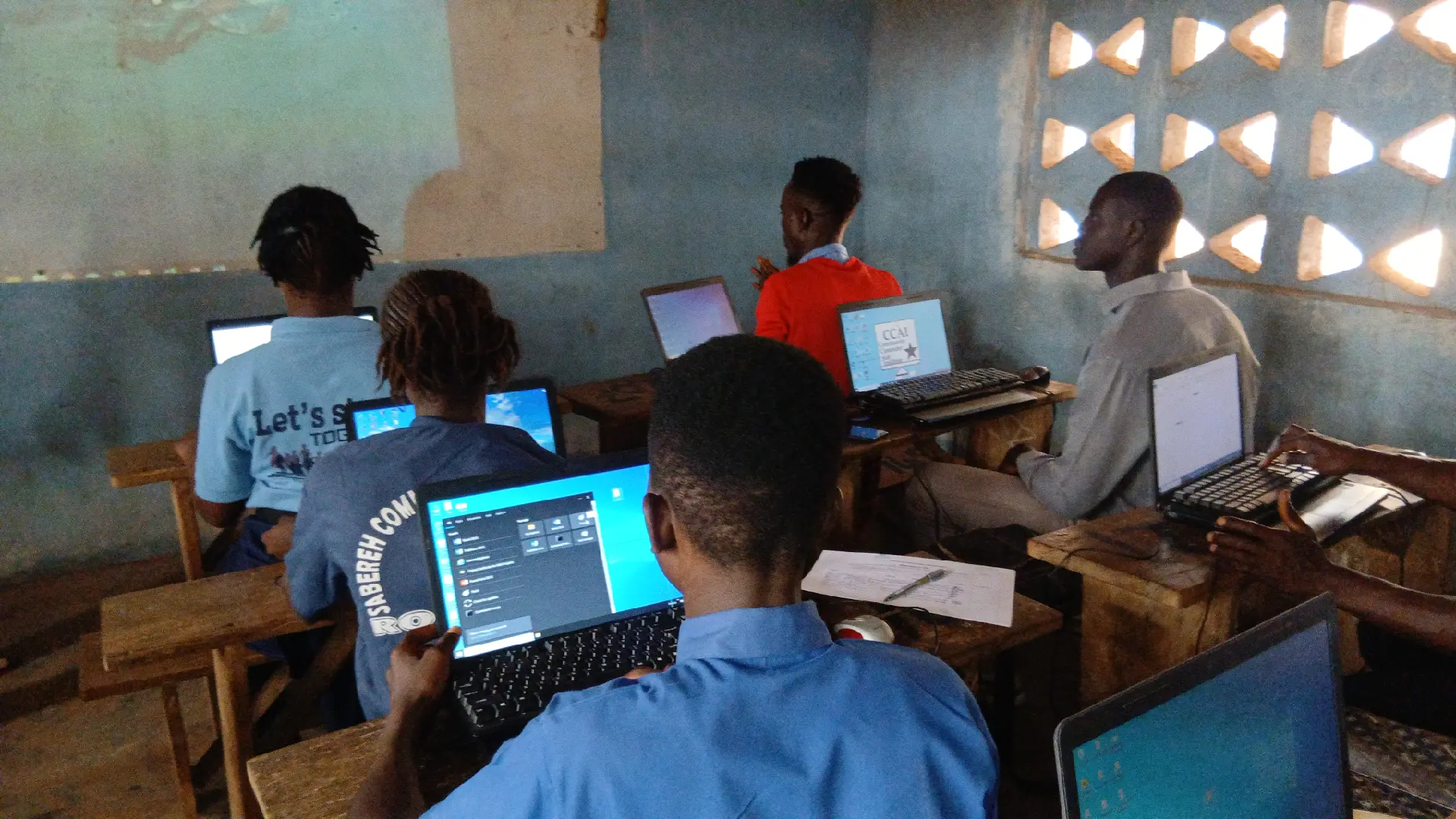 Students in school uniform working on laptops in a community classroom
