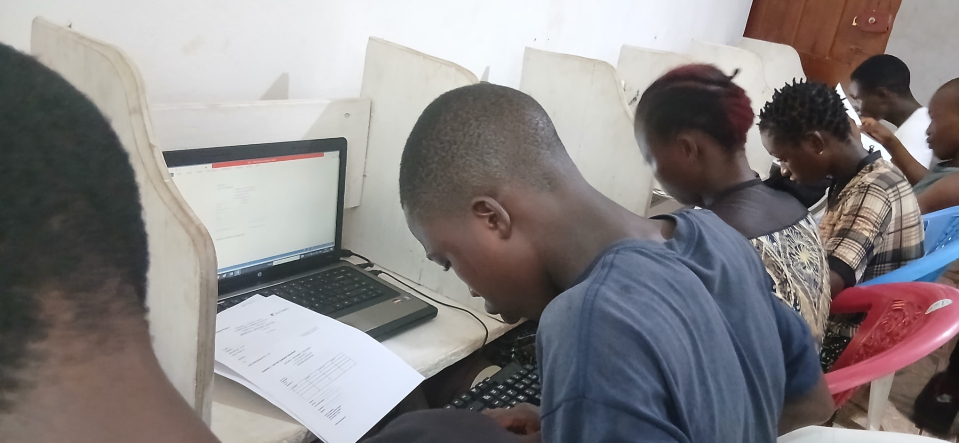 A learner following a printed worksheet while working on a Word document on a laptop