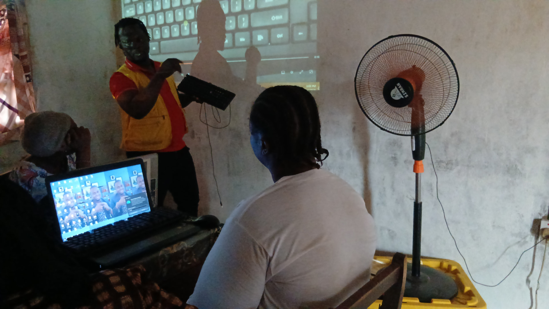 A trainer holding a keyboard and pointing at a projected keyboard diagram during an evening class