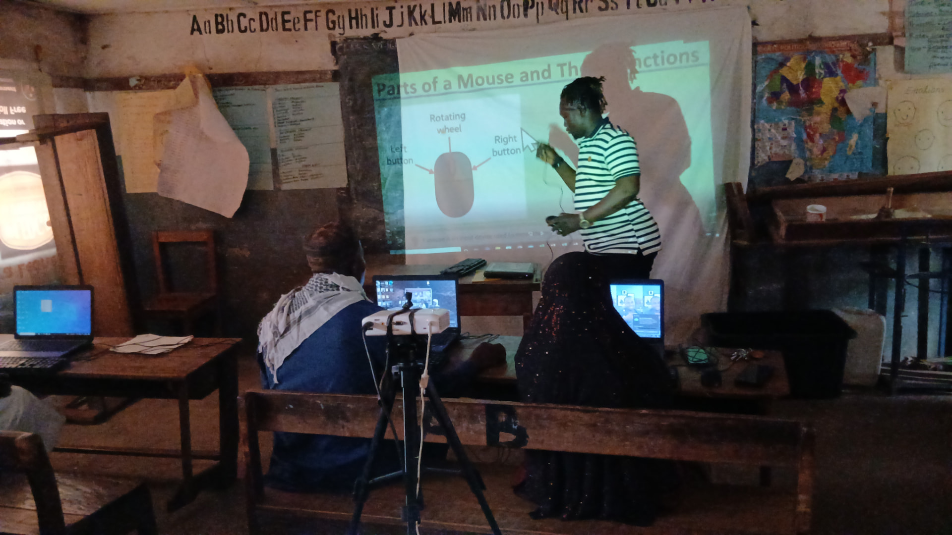 A facilitator using a projector to teach the parts of a mouse in a rural classroom