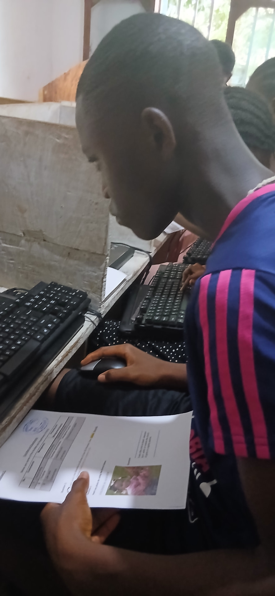 A learner using a mouse and keyboard while reading a Publisher design brief