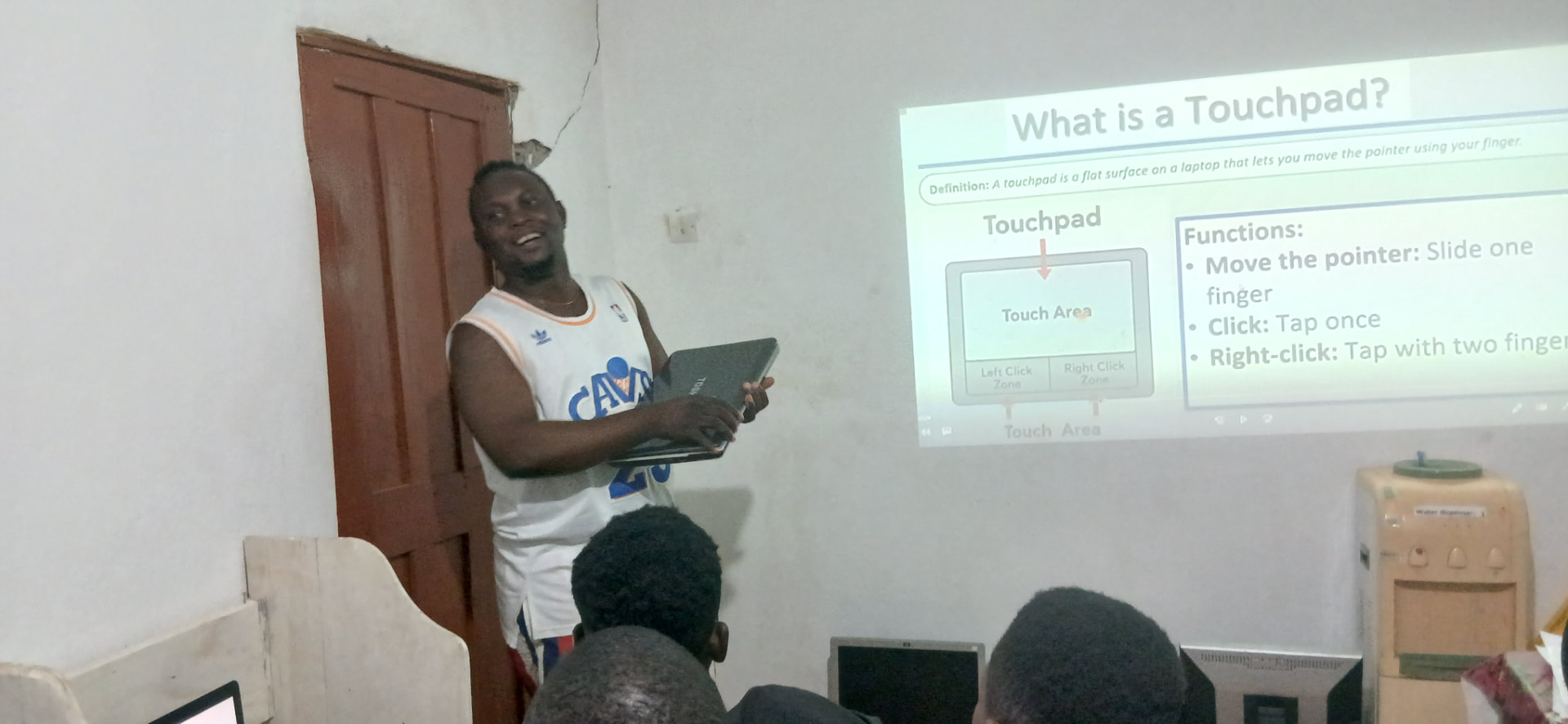 A smiling trainer holding a laptop while presenting a slide explaining the touchpad